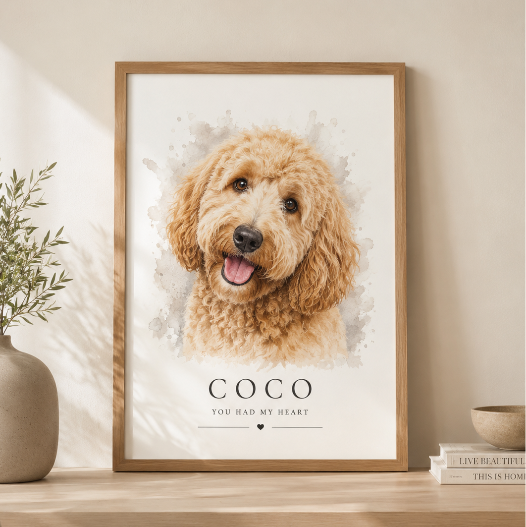A framed watercolor-style pet portrait print leaning on a light wood console table in a warm neutral room. The artwork shows a fluffy golden-brown dog, with their name below it.