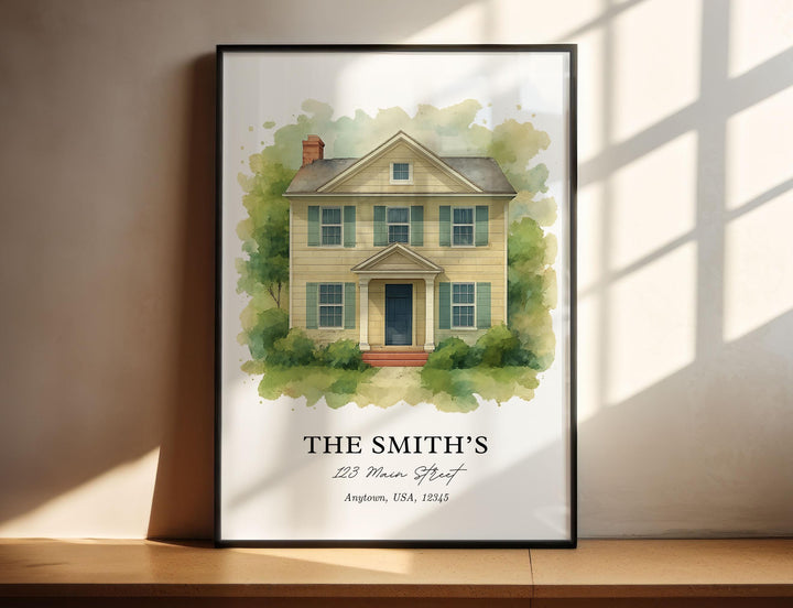 Custom watercolor house portrait print example featuring a two-story yellow home with green shutters surrounded by trees, personalized with a family name and address below, displayed in a black vertical frame.